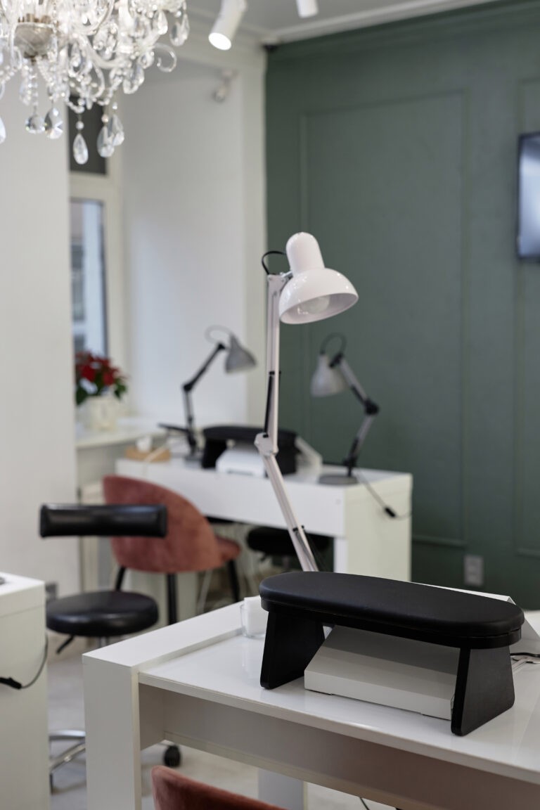 Vertical shot of manicure workplace with white table lamp. Modern bright interior design of nail salon with professional equipment, focus on lamp